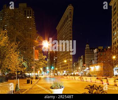 Il Flatiron Building si illumina caldo sotto i semafori sotto un cielo indaco prima dell'alba; il traffico sparso lascia sentieri leggeri nella foto di esposizione al tempo. Foto Stock