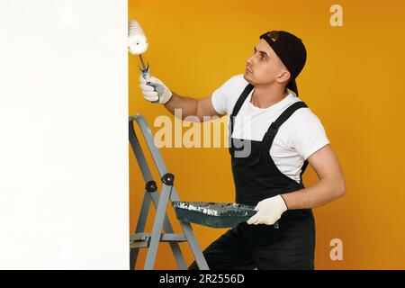 giovane uomo in abiti da lavoro dipingendo pareti bianche Foto Stock