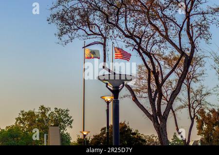 Un'interessante immagine dell'ora d'oro delle bandiere degli Stati Uniti e della California che sventolano nel vento alto su un flagpole al Crafton Hills College. Foto Stock