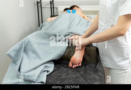 Specialista riabilitazione, fisioterapista fa massaggio ai piedi a paziente con paralisi cerebrale, scoliosi. Specialista sanitario, Riabilitazione Foto Stock