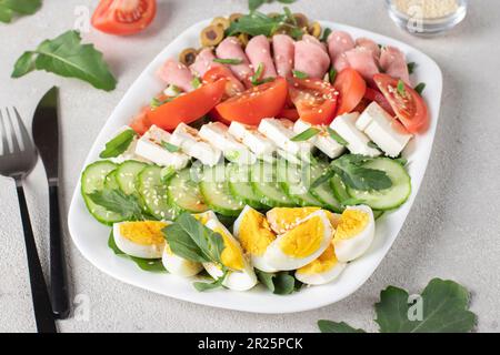 Insalata sana di cobb con prosciutto, formaggio feta, cetriolo, pomodoro, olive e uova su piatto bianco. Pranzo chetogenico Foto Stock