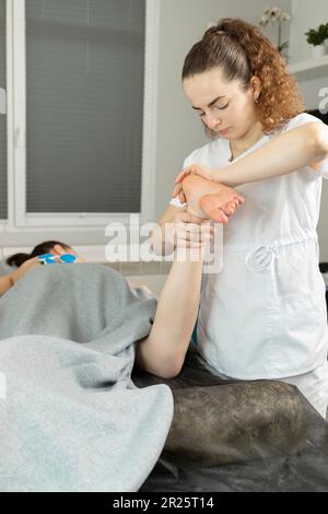 Specialista riabilitazione, fisioterapista fa massaggio ai piedi a paziente con paralisi cerebrale, scoliosi. Specialista sanitario, Riabilitazione Foto Stock