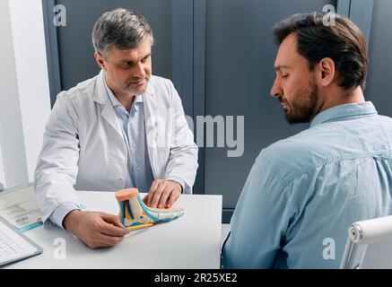 Trattamento piedi piatti. Medico podiatristo consultare l'uomo adulto con piede piatto, spiegando i metodi di trattamento utilizzando il modello plano pes anatomico Foto Stock