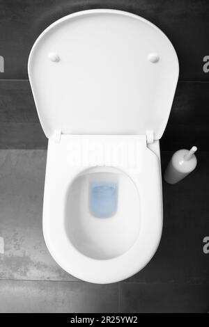 Vista dall'alto di una tazza di gabinetto bianca con un coperchio rialzato contro un pavimento in ceramica nera. Foto Stock