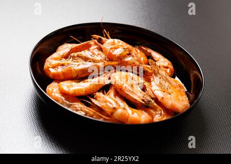 Gamberetti fritti in un piatto nero su un tavolo in ceramica scuro primo piano. Grigliata di gamberetti su sfondo scuro. Foto Stock