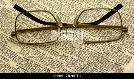 Un paio di occhiali da lettura o di occhiali su un vecchio giornale con una stampa molto piccola; tema di lettura Foto Stock