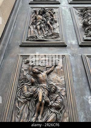 Gravina, Italia. Splendidi dettagli sulla porta d'ingresso della Cattedrale Cattolica Romana Gravina. Raffigurazione della crocifissione e del battesimo di Gesù (in alto). Foto Stock