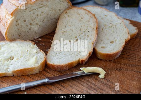 Pane affettato su un tagliere di legno, panino in pastella, mattina di routine colazione nazionale. Foto Stock