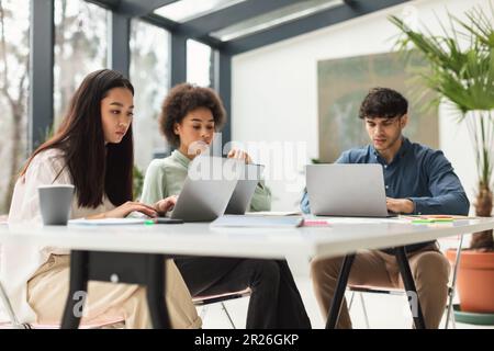Tre colleghi multietnici che lavorano utilizzando i notebook a tavolo in ufficio Foto Stock