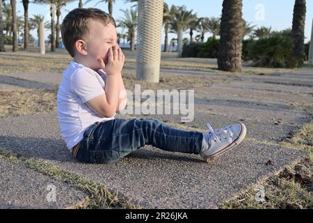 Il ragazzino caduto nel parco. sta piangendo. chiama per assistenza. Foto Stock