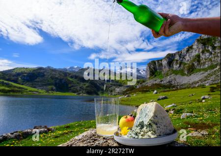 Versando in un bicchiere di sidro asturiano naturale a base di mele fermentate, il cabrales asturiano è un formaggio di mucca azzurra con vista sui laghi di Covadonga e sulle cime del Pico Foto Stock