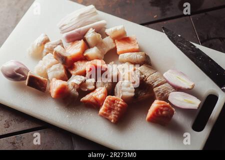 Pezzi di gru a pezzi e pesce bianco su un tagliere su sfondo scuro. Cucinare cibo. Pesce crudo. Foto Stock