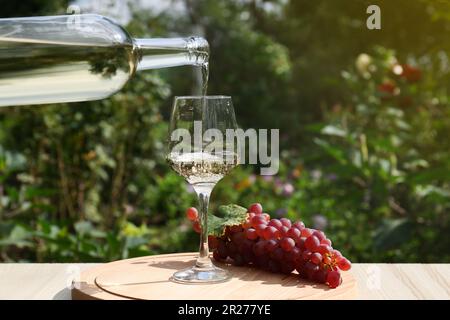 Versare vino bianco dalla bottiglia in vetro a tavola di legno all'aperto, primo piano. Spazio per il testo Foto Stock