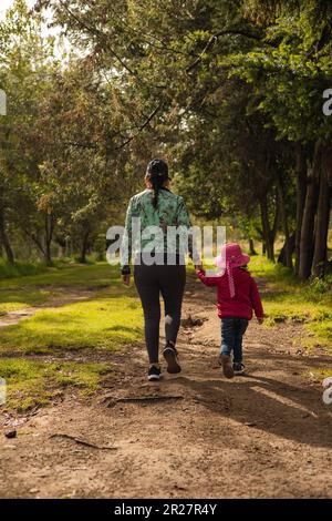 figlia piccola con la madre che fa una passeggiata durante il giorno in un parco, stile di vita familiare, cura e protezione del bambino, carta da parati con la natura Foto Stock