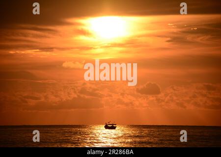 Tramonto sull'oceano con silhouette in barca. Le vivaci tonalità del sole tramontano il cielo in una sinfonia di colori caldi Foto Stock