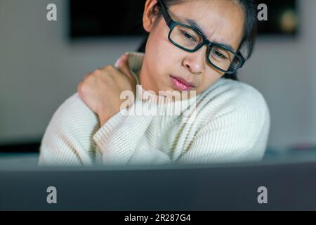 Giovane donna asiatica che sente dolore al collo e alle spalle dopo aver lavorato a lungo sul suo notebook. Concetto di sindrome dell'ufficio. Foto Stock