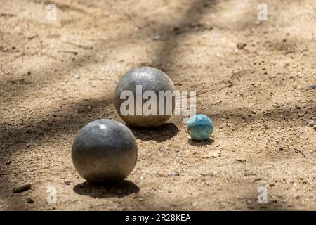 Due palle di metallo dal gioco di petanque avvicinarsi alla palla da bowling su un terreno sabbioso di un campo di petanque in una giornata di sole con le ombre del tr Foto Stock