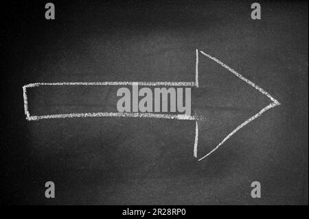 Freccia bianca disegnata su una tavola nera con gesso che indica una direzione Foto Stock