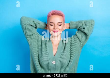 Foto di giovane rilassata ragazza addormentata accogliente indossare alla moda mani cardigan testa nap rosa tinto capelli corti isolato su sfondo di colore blu Foto Stock