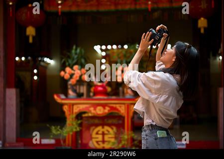 Felice giovane turista asiatico femmina scattando foto di un tempio cinese, godendo il suo punto di riferimento turistico della città. Foto Stock