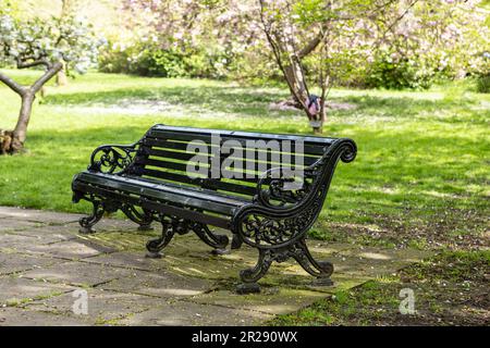 Panca in legno con ferro battuto e gambe in metallo di colore nero nel  cestino nel parco su uno sfondo di prato verde e al tramonto Foto stock -  Alamy