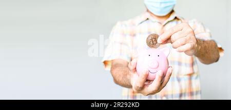 Una mano di un uomo che tiene una moneta bitcoin per far cadere la banca rosa del maialino. il concetto di risparmio di denaro sotto forma di bitcoins che danno maggiori rendimenti. Selettivo foc Foto Stock