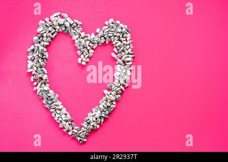 Simbolo del cuore costituito da piccole pietre o ciottoli posti su sfondo rosa. È un concetto di giorno d'amore o di giorno di San Valentino. Vista dall'alto e primo piano Foto Stock