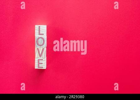Scatta un primo piano. Le lettere 'AMORE' sul cubo di legno sono disposte verticalmente su uno sfondo rosso. Concetto di Love Day o San Valentino Foto Stock