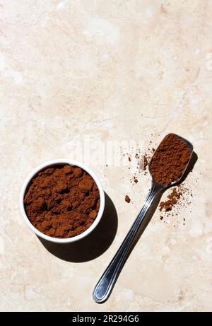 Ciotola bianca in ceramica e un cucchiaio d'argento riempito di caffè macinato su un tavolo di marmo chiaro in una mattinata di sole. Caffè macinato arrosto isolato su erba leggera Foto Stock