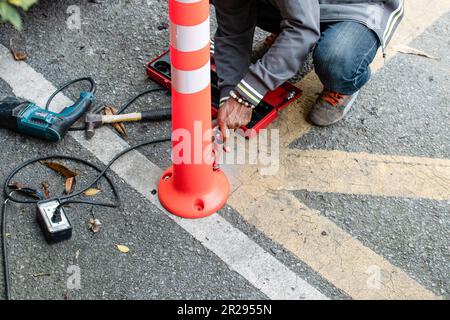 Primo piano un uomo sta lavorando installando un piccolo cono stradale sulla strada, una mano dell'uomo che tiene una chiave a blocchetto per avvitare il dado alla strada. Strumenti per Foto Stock