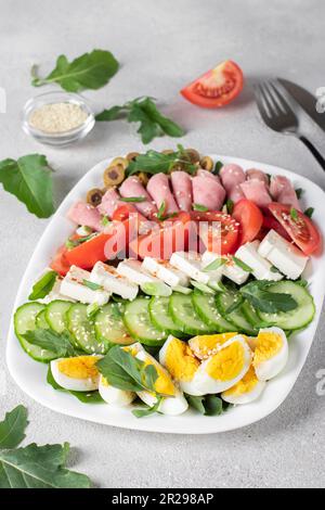 Insalata sana di cobb con prosciutto, formaggio feta, cetriolo, pomodoro, olive e uova su piatto bianco. Pranzo chetogenico Foto Stock