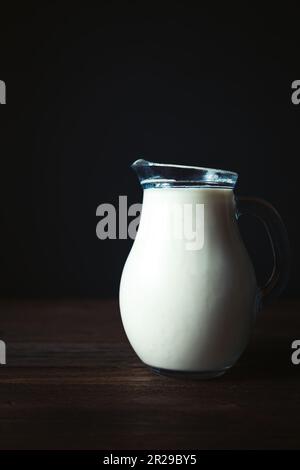 Caraffa piena di latte sul tavolo di legno. Prodotto agricolo, sfondo nero, spazio copia. Foto Stock