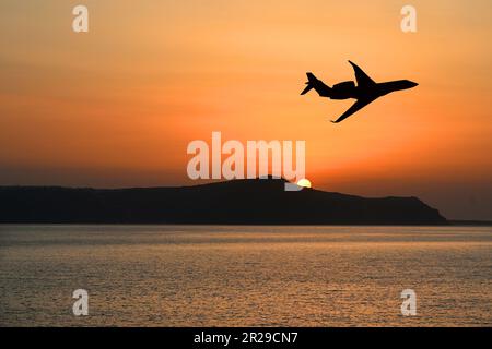 Silhouette di un jet privato executive che sorvola un'isola al tramonto. Concetto di viaggio di lusso. Spazio di copia. Nessuna gente. Foto Stock