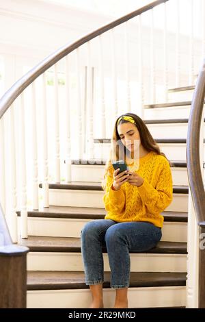 Donna caucasica premurosa seduta sulle scale a casa utilizzando lo smartphone, con spazio copia Foto Stock
