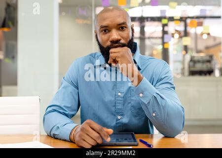 Ritratto di uomo d'affari afro-americano con mano sul mento seduto alla scrivania in ufficio Foto Stock