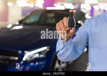 Chiavi dell'auto. Mano maschile che tiene la chiave dell'auto, su uno sfondo di parcheggio Foto Stock