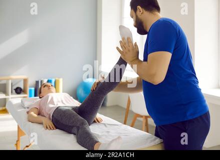 Il fisioterapista esamina la gamba del paziente e gli esercizi con lei durante la terapia riabilitativa. Foto Stock