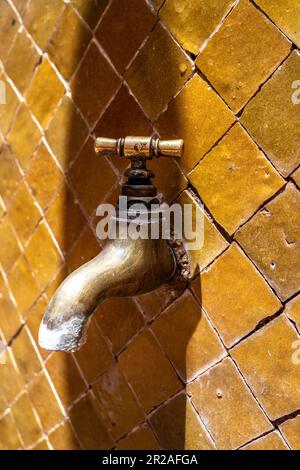 Vecchio rubinetto d'acqua in ottone isolato su uno sfondo piastrellato color ambra. valvola del rubinetto. vecchio rubinetto in ottone retro,. tubazioni, riparazioni,. Primo piano vintage Foto Stock