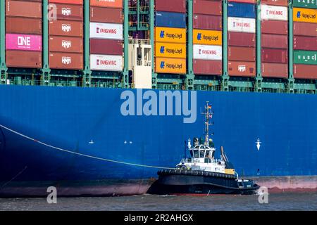 Amburgo, Germania - 04 17 2023: Vista del lato della nave di una nave container con container e un rimorchiatore davanti ad essa Foto Stock