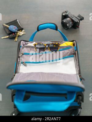 Piccola borsa blu con occhiali da sole, fotocamera, portafoglio e chiavi per una vacanza breve. Posa su un pavimento in cemento. Foto Stock