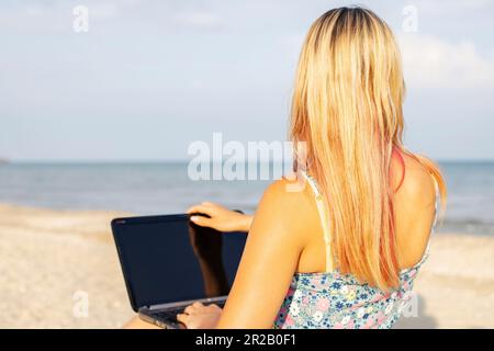 Bella donna con computer portatile in spiaggia. Lavorare in remoto sulla riva del mare Foto Stock