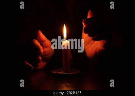 le mani della vecchia donna e la fiamma della candela al buio, la luce della candela, il lutto, la candela al buio Foto Stock