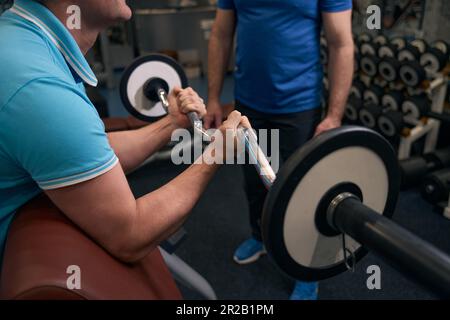 Tipo sportivo che esegue l'esercizio del bicipite sotto la supervisione di allenatore di fitness Foto Stock