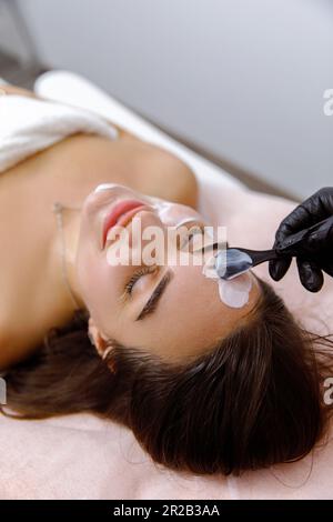Trattamento viso, coccole viso, procedura cosmetica, purificatio della pelle, scrubbing della pelle, Trattamenti di bellezza, servizi di dermatologia, procedura di sollevamento. Il cosmetologo applica la crema al volto di una giovane donna Foto Stock