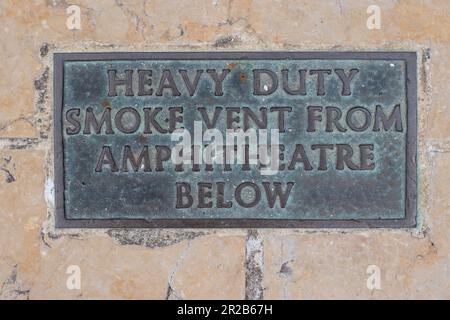 Scarico di fumo per impieghi pesanti dall'anfiteatro sotto la placca di bronzo con segno di bronzo sul marciapiede del marciapiede nella City of London Foto Stock
