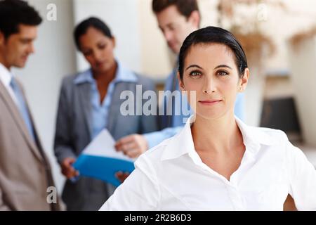 Shes serio circa successo. Ritratto di una bella giovane donna d'affari con i suoi colleghi sfocato sullo sfondo. Foto Stock