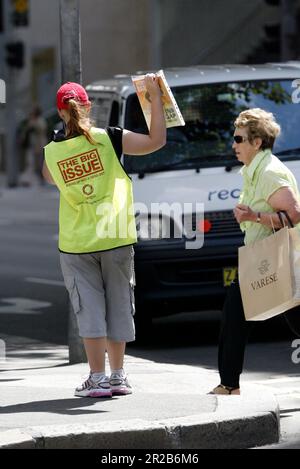 Un venditore di strada che vende The Big Issue, una rivista quindicinale che presenta gli affari attuali, l'intrattenimento, la fotografia e il commento, venduto per le strade di città e città in tutta l'Australia da persone che vivono senza casa o disoccupazione di lunga durata. Aiuta le persone ad aiutare se stesse, poiché i fornitori mantengono la metà del prezzo di copertura di $5 dollari di ogni rivista che vendono. Posizione: All'angolo tra Elizabeth e King Street, Sydney. Foto Stock