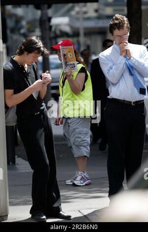 Un venditore di strada che vende The Big Issue, una rivista quindicinale che presenta gli affari attuali, l'intrattenimento, la fotografia e il commento, venduto per le strade di città e città in tutta l'Australia da persone che vivono senza casa o disoccupazione di lunga durata. Aiuta le persone ad aiutare se stesse, poiché i fornitori mantengono la metà del prezzo di copertura di $5 dollari di ogni rivista che vendono. Posizione: All'angolo tra Elizabeth e King Street, Sydney. Foto Stock