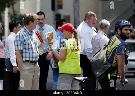 Un venditore di strada che vende The Big Issue, una rivista quindicinale che presenta gli affari attuali, l'intrattenimento, la fotografia e il commento, venduto per le strade di città e città in tutta l'Australia da persone che vivono senza casa o disoccupazione di lunga durata. Aiuta le persone ad aiutare se stesse, poiché i fornitori mantengono la metà del prezzo di copertura di $5 dollari di ogni rivista che vendono. Posizione: All'angolo tra Elizabeth e King Street, Sydney. Foto Stock