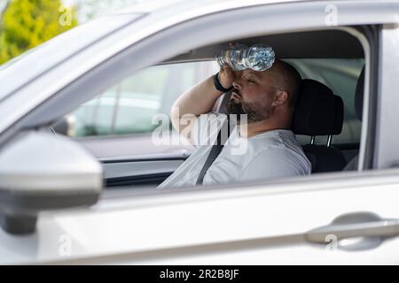 L'uomo stanco e sovrappeso guida l'auto con aria condizionata rotta in estate caldo tempo. Foto Stock